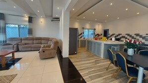 A modern living room with a sectional sofa, a dining area with a table and chairs, and a kitchen with a tiled backsplash. - Butterfly House (Malindi)