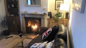 A cozy living room with a fireplace, a leather sofa with British flags, a wooden coffee table, and a bookshelf. - Beautiful Sea Front Cottage in the Ocean City (Plymouth)