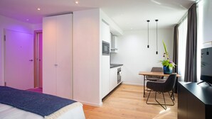 Una habitación de hotel moderna con una cama, un escritorio, una silla, un televisor, una zona de cocina y un baño.