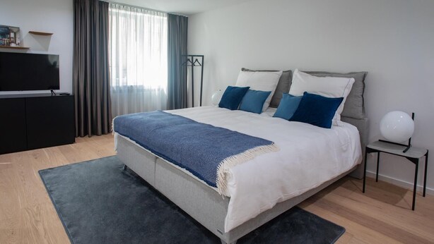 Un dormitorio moderno con una cama grande, un televisor de pantalla plana y una mesita de noche con lámpara.
