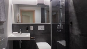 Un baño moderno con ducha de vidrio, lavamanos blanco y retrete.