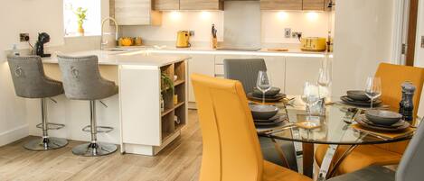 A modern kitchen with wooden cabinets, a central island, bar stools, and a dining table set for four.