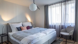 A modern bedroom with a large bed, bedside tables, a chair, and a window with curtains.