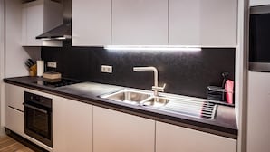A modern kitchen with a stainless steel sink, a built-in oven, and a black backsplash.