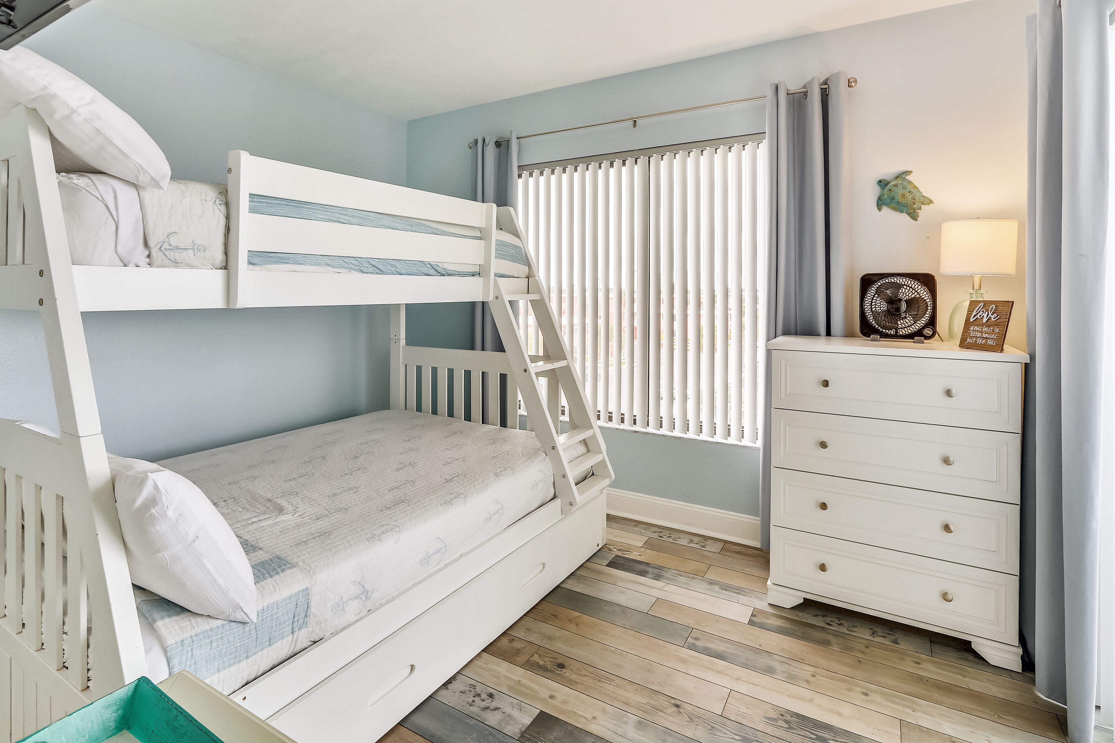 Une chambre avec un lit superposé, une commode et une fenêtre équipée de stores.
