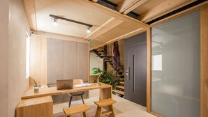 A modern office space with a wooden desk, two stools, a laptop, and a staircase leading to a balcony. - Thallos the Boutique (Chania)