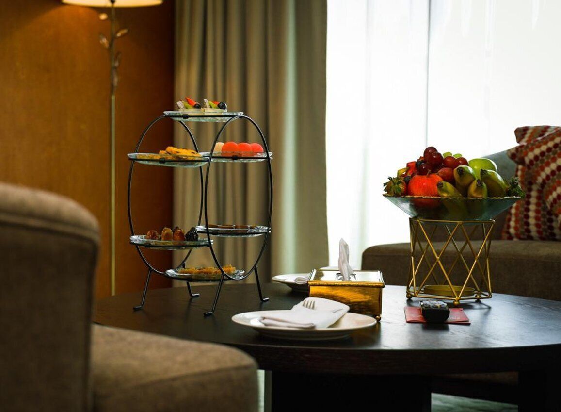 A dining area with a three-tiered dessert stand, a bowl of fruit, and a table set with plates and cutlery.