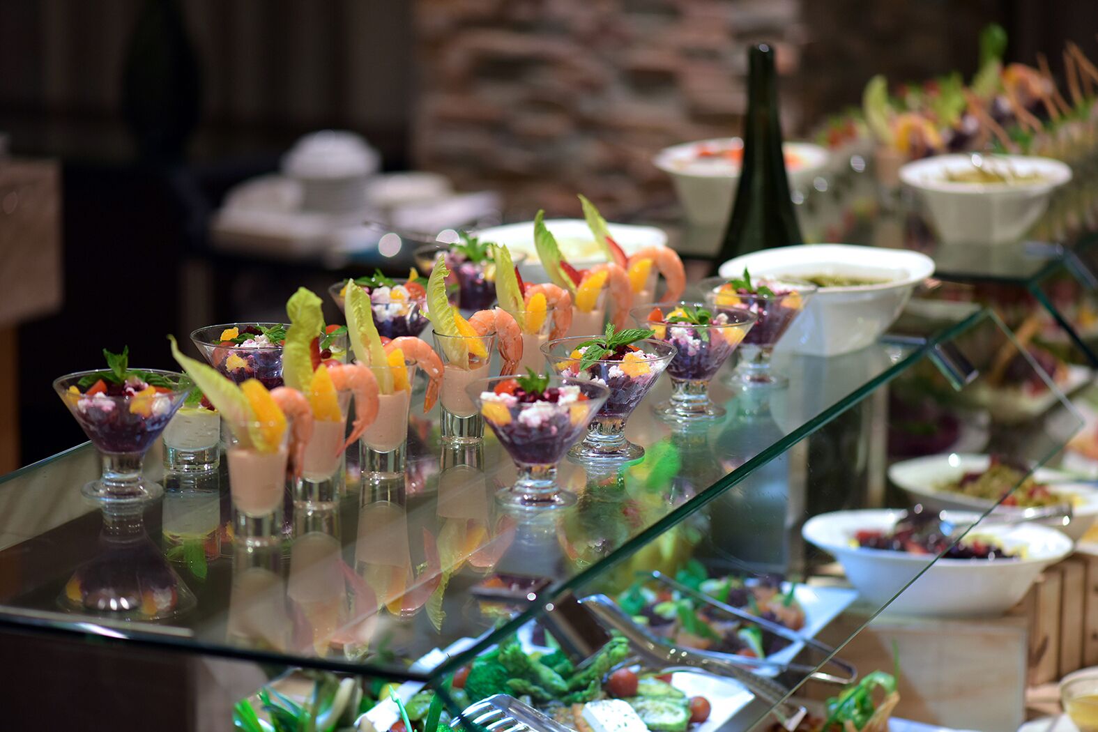 A buffet with various dishes, including shrimp cocktails and fruit salads, displayed on a glass counter.