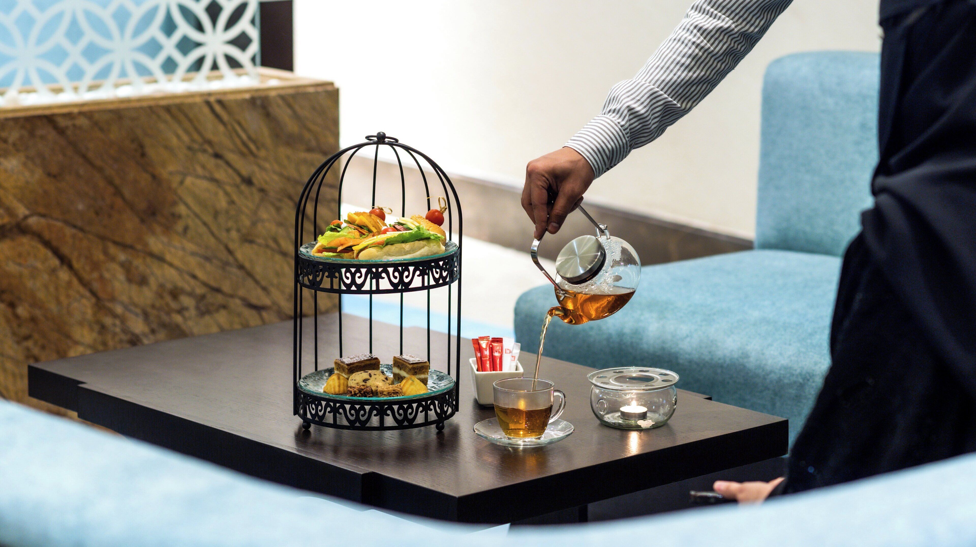 A tray with a dessert stand, a glass of tea, and a candle on a table.