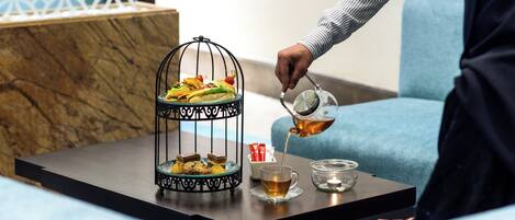 A tray with a dessert stand, a glass of tea, and a candle on a table.