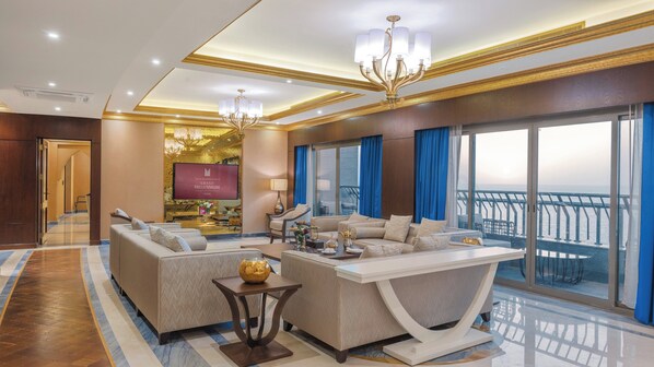 A spacious living room with a large TV, comfortable seating, and a balcony with a view.