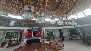 Amplia habitación con techo de paja, lámparas colgantes y una mesa central con sillas.