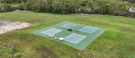 An outdoor tennis court with four courts, surrounded by grass and trees.