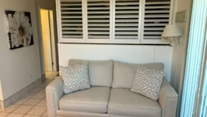 Ein beiges Sofa mit gemusterten Kissen, eine Wand-Klimaanlage und eine Stehlampe.