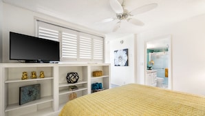 Ein Schlafzimmer mit einem Bett, einem Fernseher auf einem Regal und einem Deckenventilator.