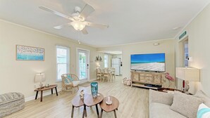 Una sala de estar amplia con ventilador de techo, un comedor con mesa y sillas, un televisor de pantalla plana grande y una zona de estar acogedora con sofá y reposapiés.