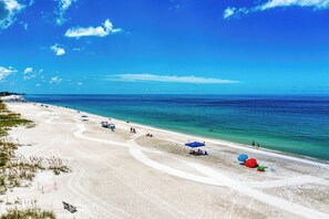 A wide sandy beach with clear blue water, a few umbrellas, and people enjoying the beach.