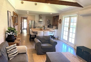 A spacious living area with a gray sofa, a gray armchair, and a coffee table. A kitchen with white subway tiles and a brick accent wall is visible in the background.
