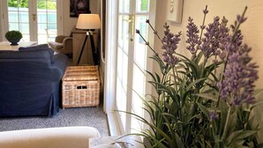 Une pièce comprenant un canapé, une lampe, un panier en osier et une grande fenêtre donnant sur un paysage verdoyant.