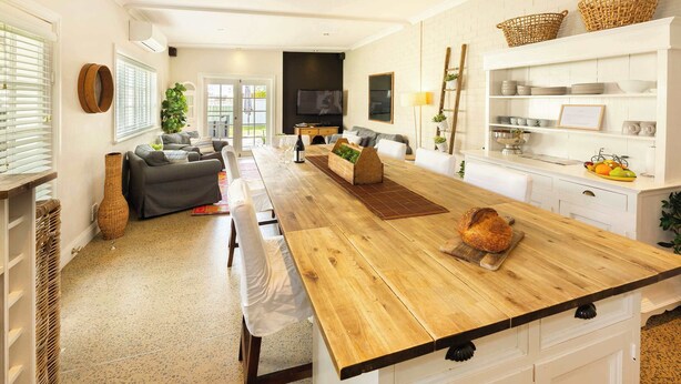 Une cuisine moderne avec un îlot central en bois, des meubles blancs et un téléviseur placé au-dessus de l’îlot.
