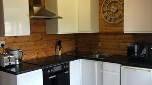 A kitchen with white cabinets, a black countertop, a stainless steel sink, a clock on the wall, and a coffee maker. - Snowdonia Log Cabin-sleeps 4-garden-pets (Blaenau Ffestiniog)