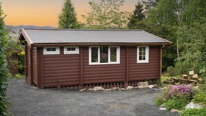 A small, single-story wooden cabin with a sloped roof, two windows, and a gravel driveway. - Snowdonia Log Cabin-sleeps 4-garden-pets (Blaenau Ffestiniog)
