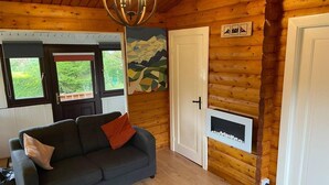 A cozy log cabin room with a dark gray sofa, a white door, and a fireplace. - Snowdonia Log Cabin-sleeps 4-garden-pets (Blaenau Ffestiniog)