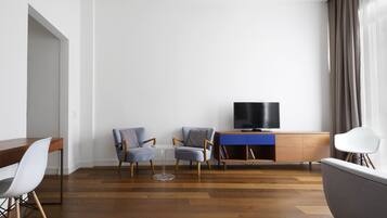 Una sala de estar moderna con piso de madera, una mesa de comedor con sillas, un televisor sobre un mueble de madera y un ventanal con cortinas.