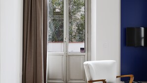 Una habitación moderna con suelo de madera, una silla blanca, un ventanal con cortinas y una pared azul decorativa.