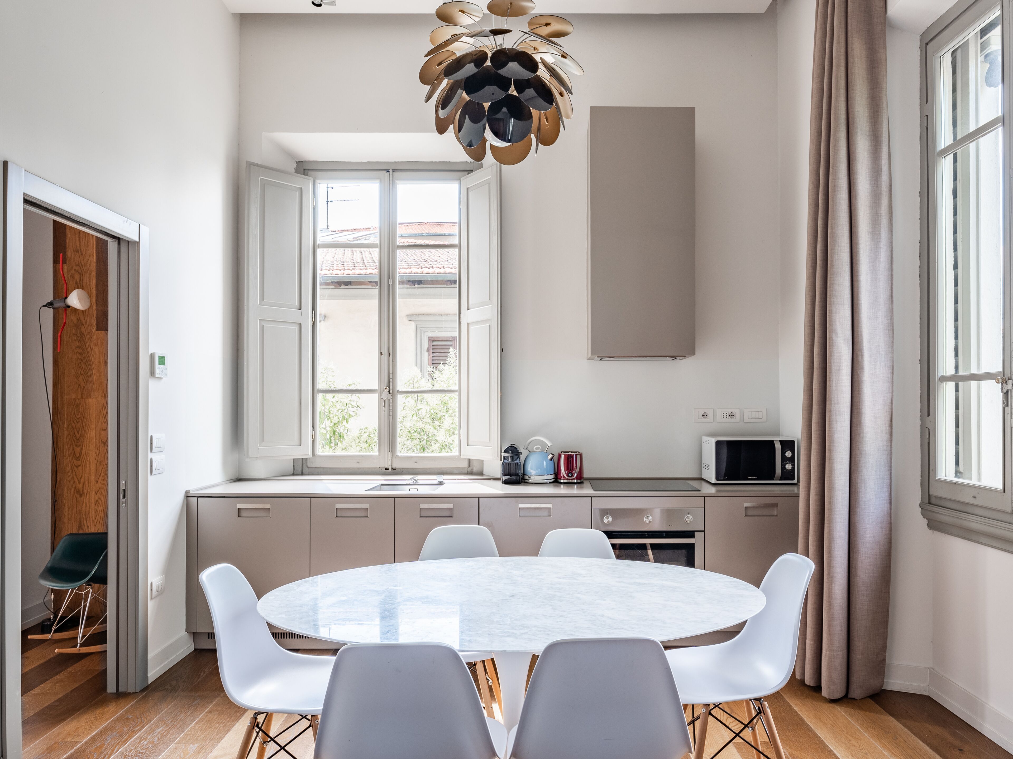 Een moderne keuken met een ronde eettafel, witte stoelen en een bijzondere kroonluchter.