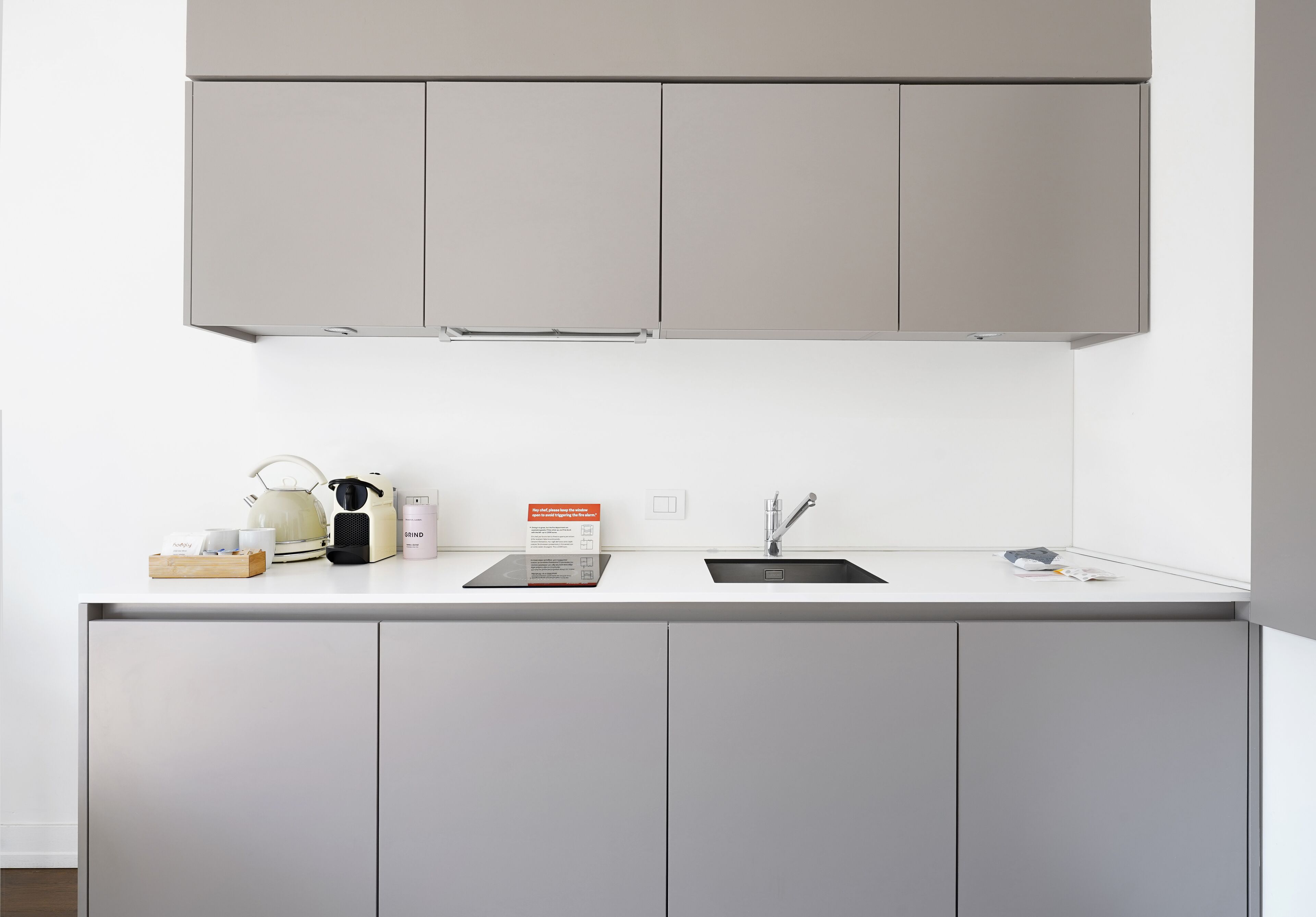 Une cuisine moderne avec des meubles gris, un plan de travail blanc et un évier en acier inoxydable.