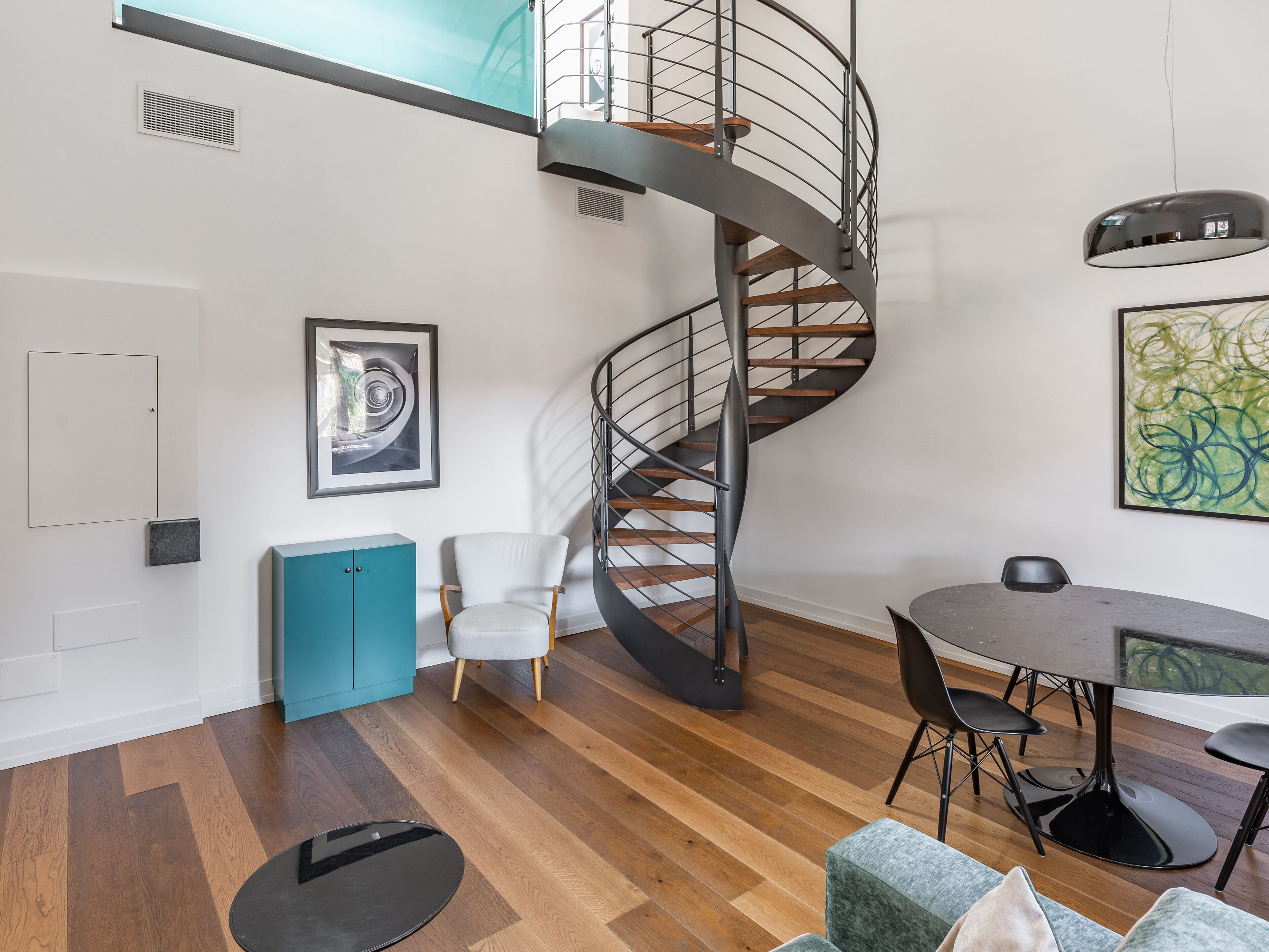 Un interior moderno con una escalera de caracol, un comedor y un armario azul verdoso.