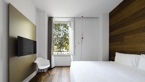 Un dormitorio moderno con una cama grande, un televisor de pantalla plana montado en la pared, una ventana con vista a árboles y una pared de acento de madera.