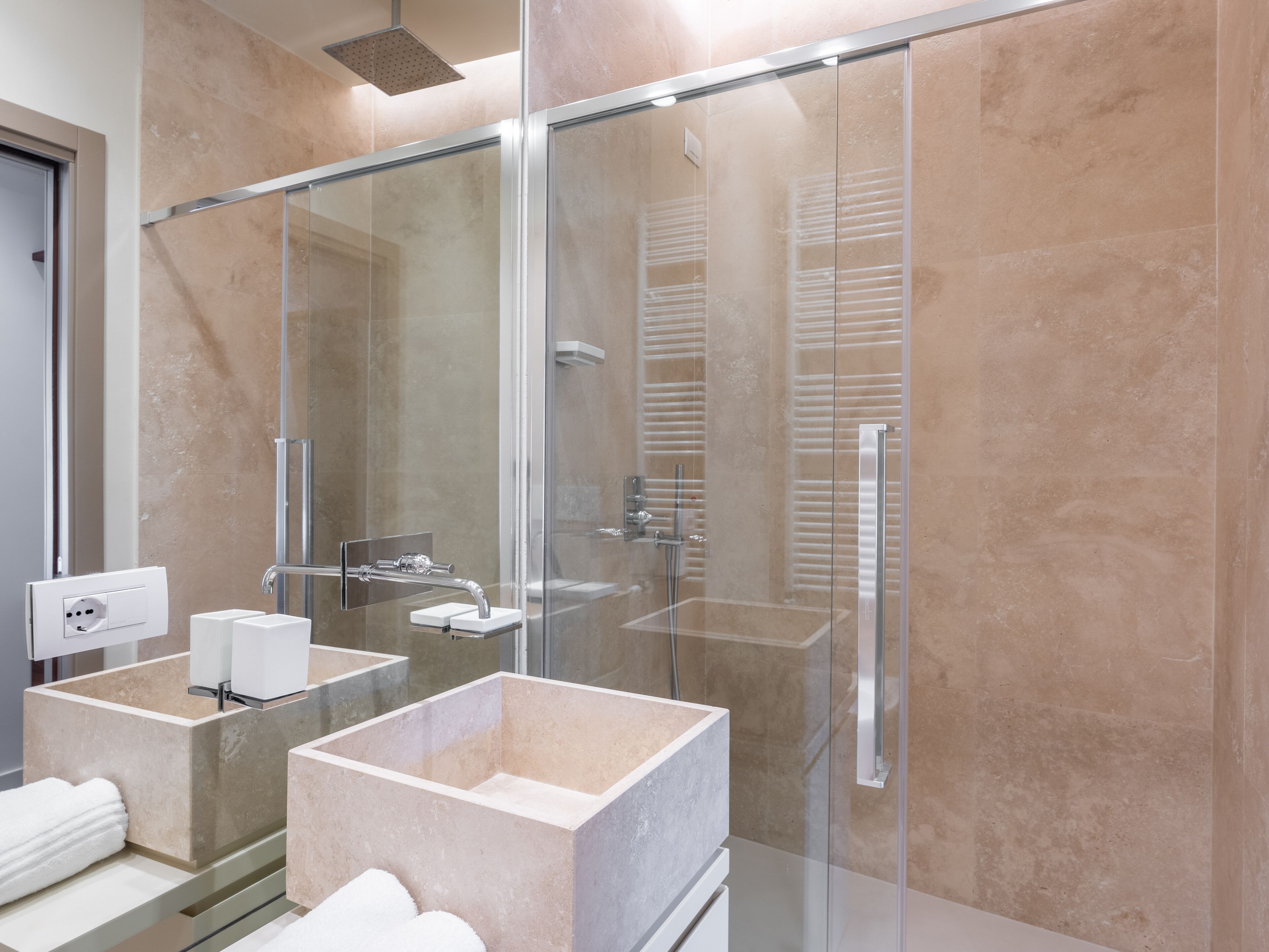 Une salle de bain moderne avec deux grands lavabos encastrés dans des parois de verre, une douche à l’italienne avec des parois de verre et un porte-serviettes apparent.