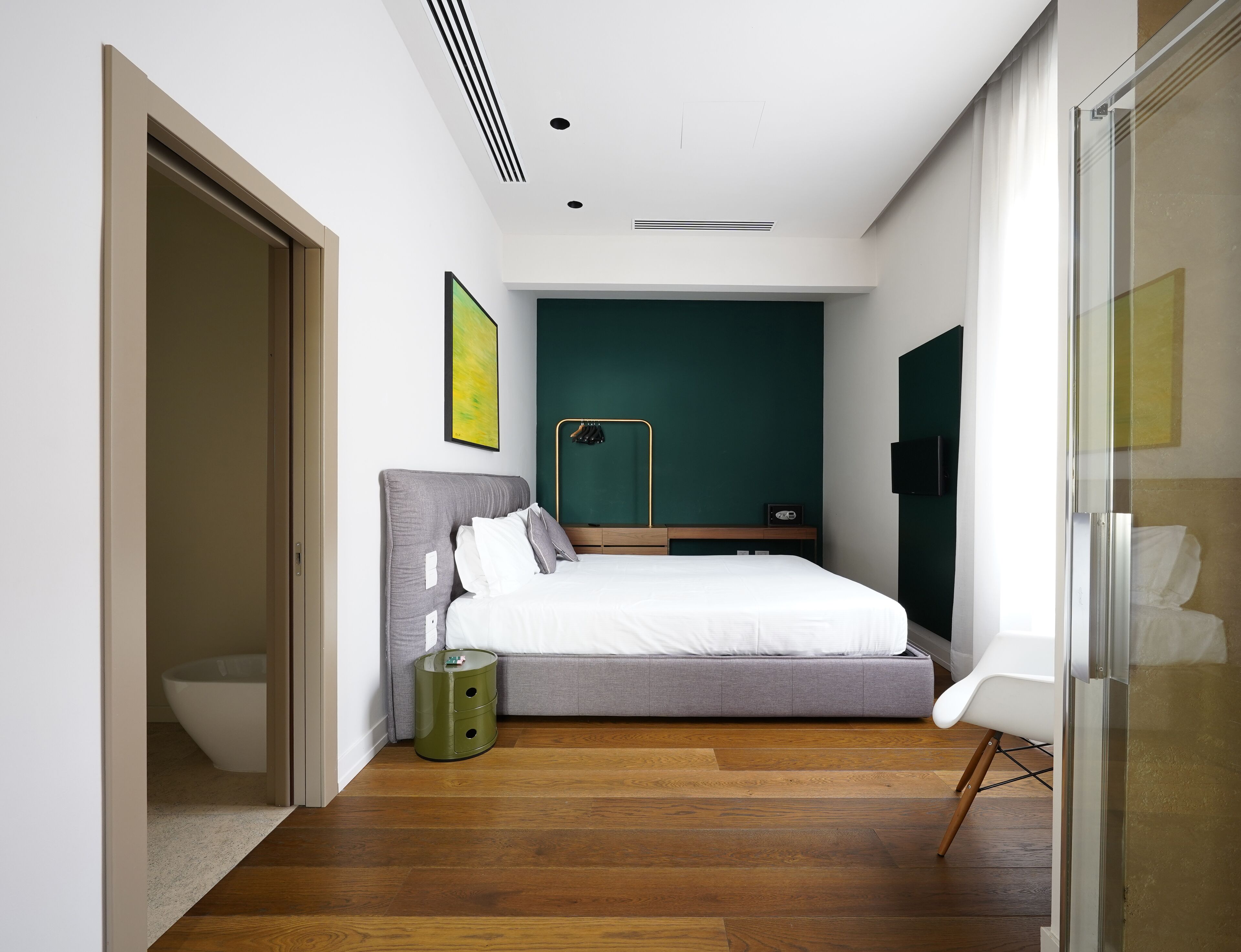Une chambre à coucher moderne avec un grand lit, une table de chevet, une poubelle verte et un téléviseur fixé au mur.