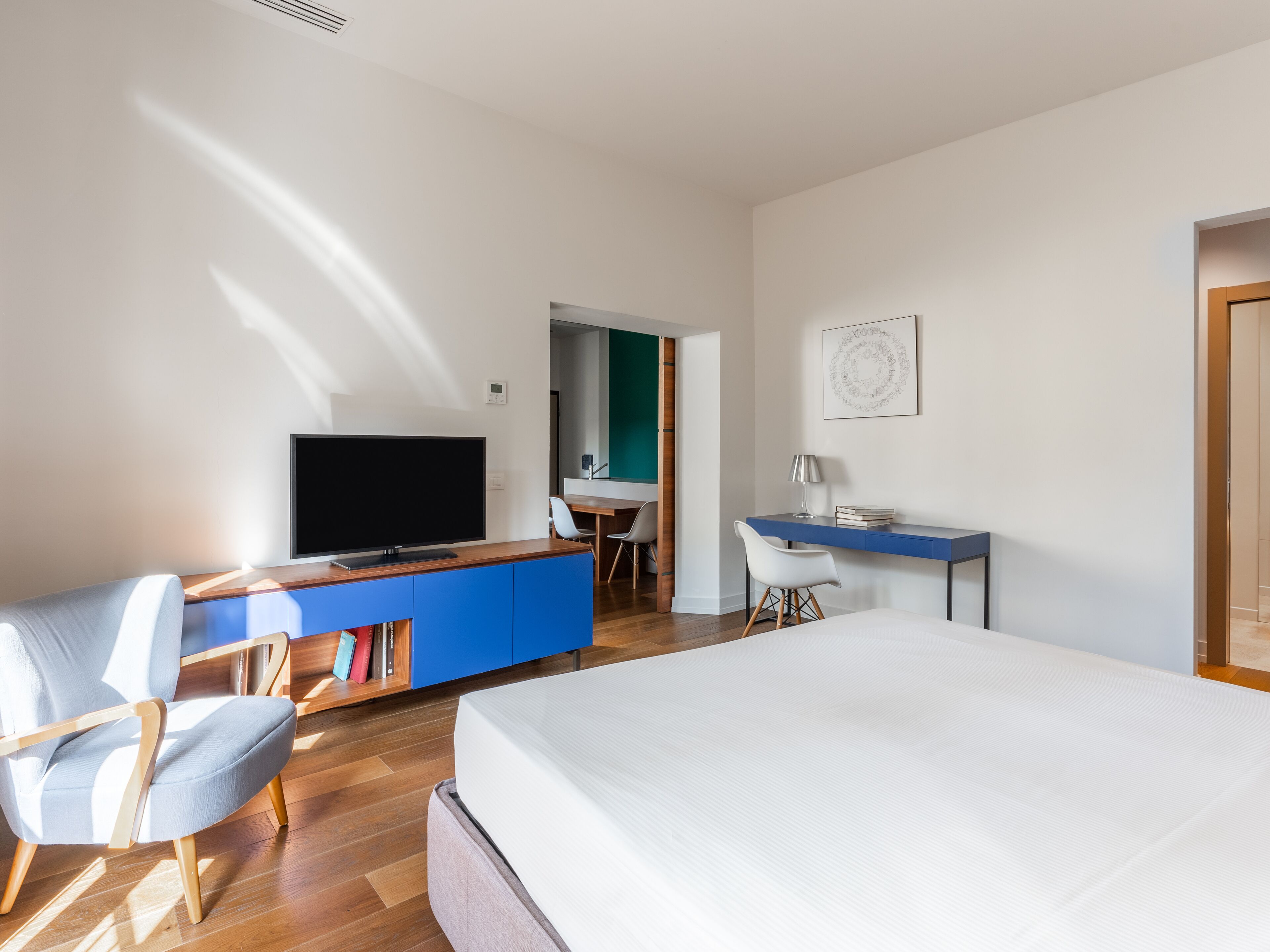 A modern hotel room with a large bed, a TV, a desk, and a chair.