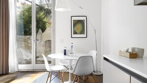 Una cocina moderna con encimera blanca, una mesa redonda de comedor con sillas blancas y un ventanal con vistas a zonas verdes.