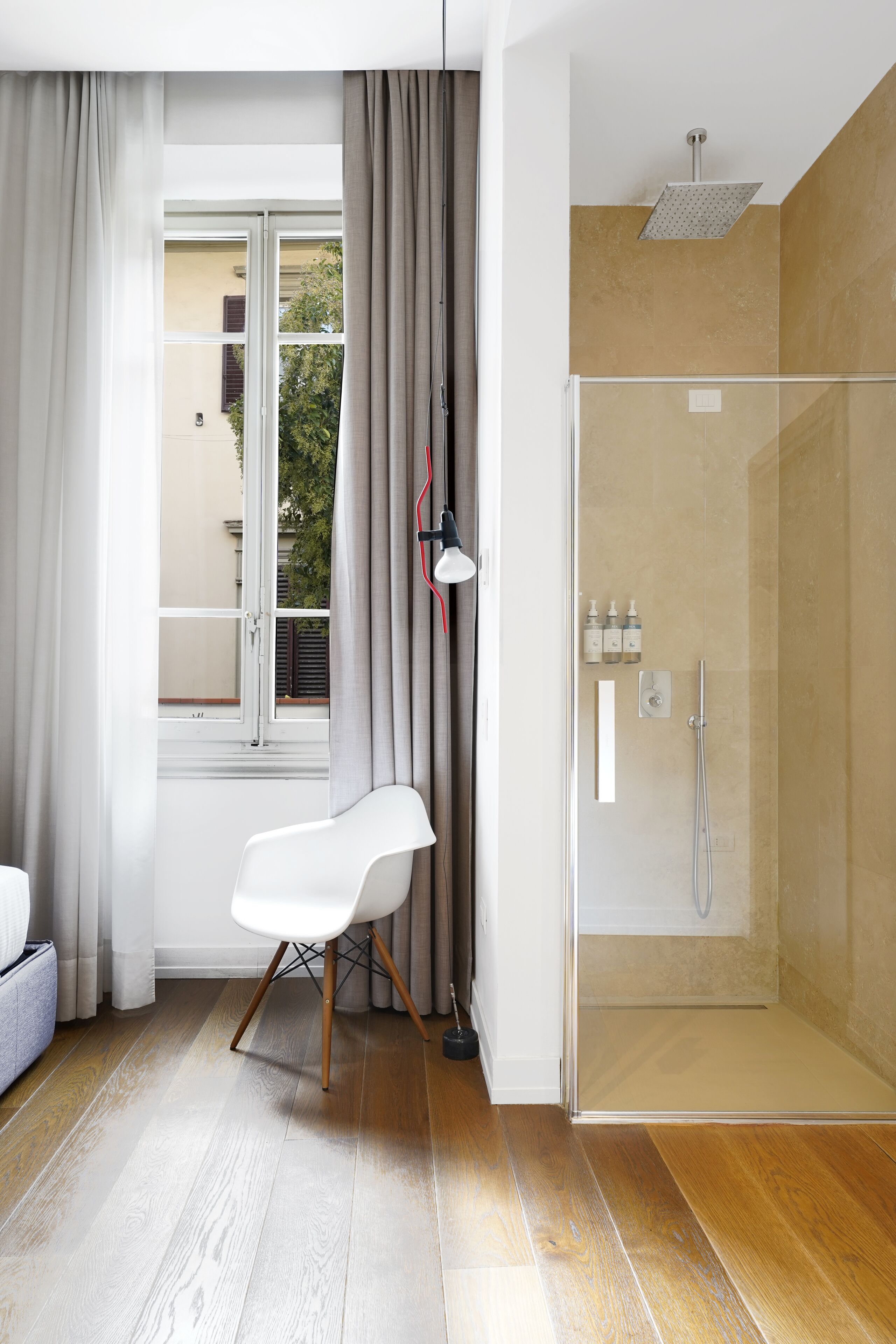 A modern bathroom with a glass shower enclosure, a white chair, and a window with curtains.