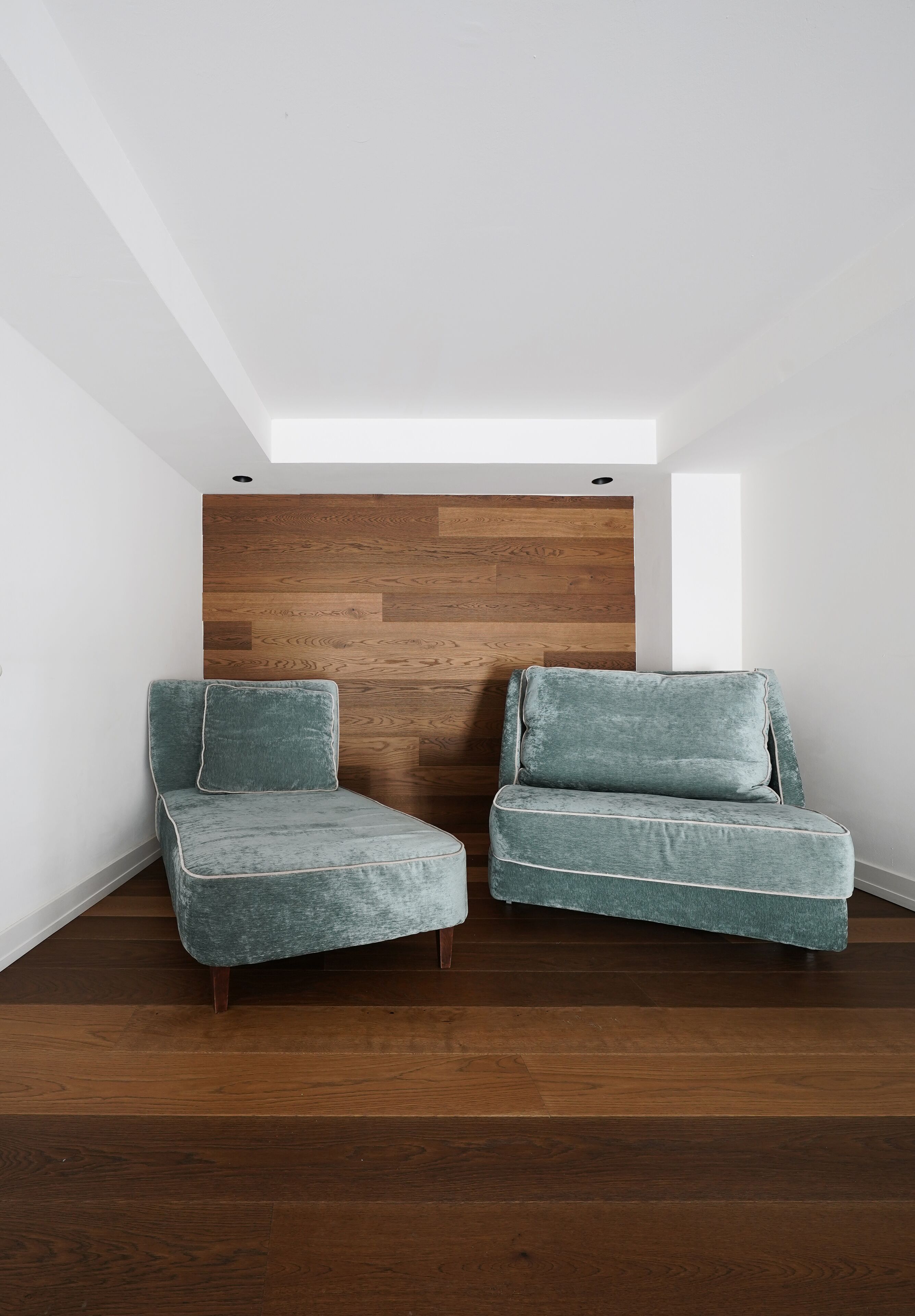 Une pièce avec deux fauteuils de couleur turquoise, un mur d’accent en bois et une lucarne.