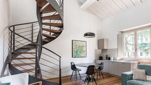 Un interior moderno con una escalera espiral, piso de madera, un comedor con sillas, un sofá y una cocina con armarios.