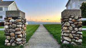 A pathway flanked by stone pillars leading to a house with a view of the sunset.