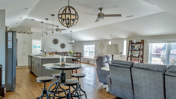 A spacious kitchen with a central island, a dining area with a round table, and a grey sofa.