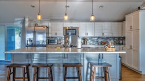 A modern kitchen with stainless steel appliances, a large island with stools, and pendant lighting.