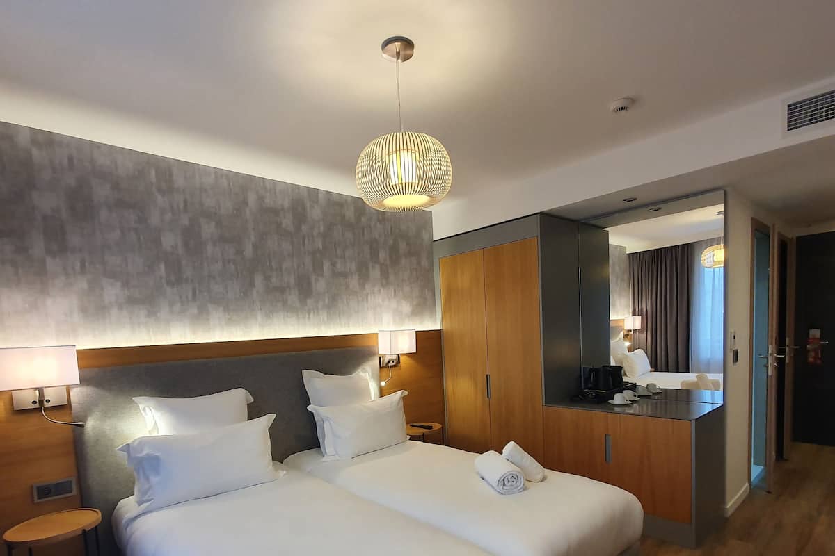 A modern hotel room with a large bed, a small desk, a mirror, and a wardrobe.
