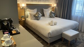 A modern hotel room with a large bed, a bedside table with a coffee maker, and a small table with tea cups and snacks. - Brit Hotel Paris Orly (Thiais)