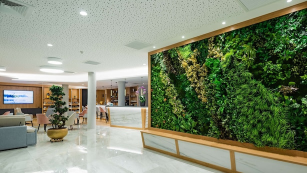 A modern lobby with a large green vertical garden, a marble reception desk, and a seating area with sofas and chairs. - Brit Hotel Paris Orly (Thiais)
