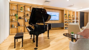 A modern living room with a grand piano, wooden shelves with various items, a television, and a wine collection. - Brit Hotel Paris Orly (Thiais)