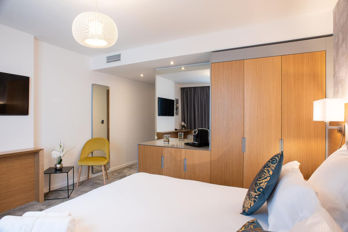 A modern hotel room with a large bed, a wooden wardrobe, a small desk, and a yellow chair.