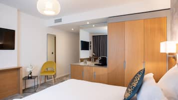 A modern hotel room with a large bed, a wooden wardrobe, a small desk, and a yellow chair.
