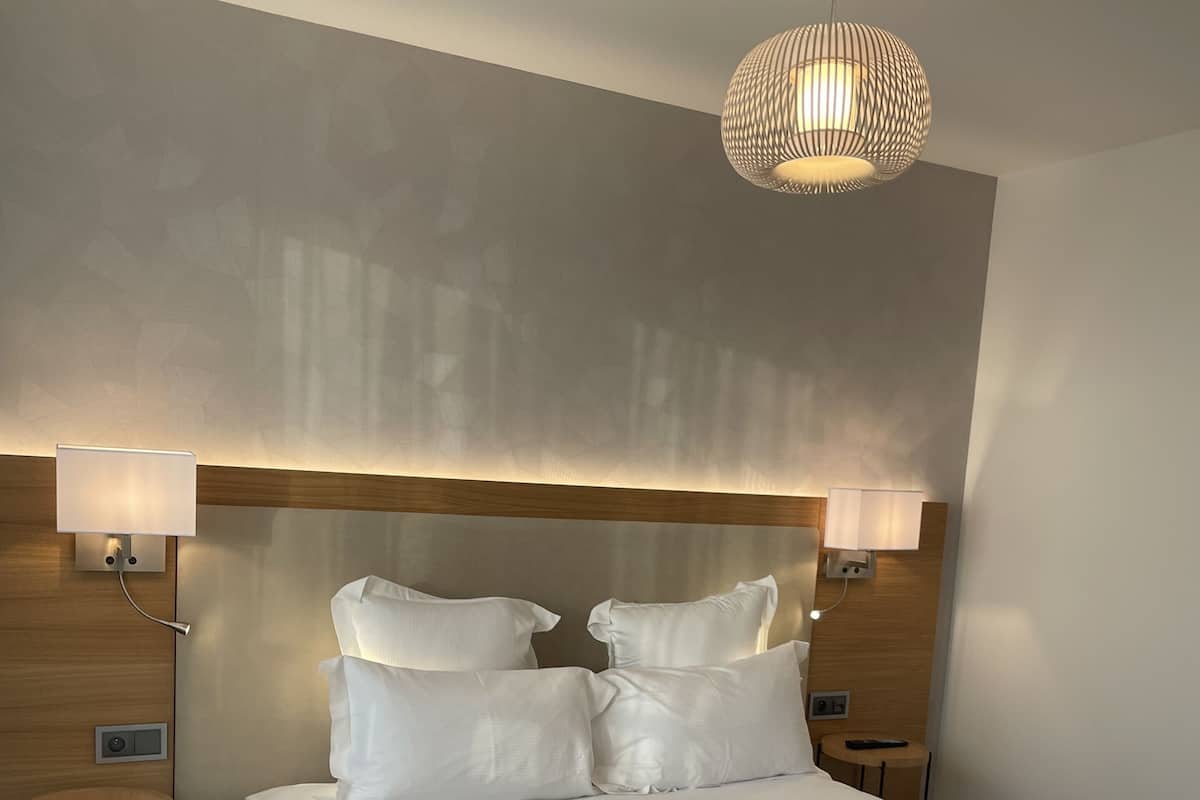 A neatly made bed with white linens, two bedside lamps, and a hanging light fixture.